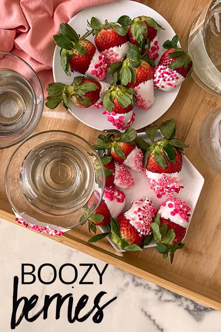 two plates with strawberries on them sitting on a table next to glasses and water