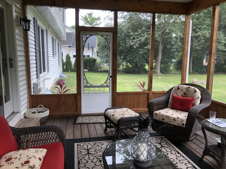 a porch with wicker furniture and red cushions on the back deck, looking out onto the yard