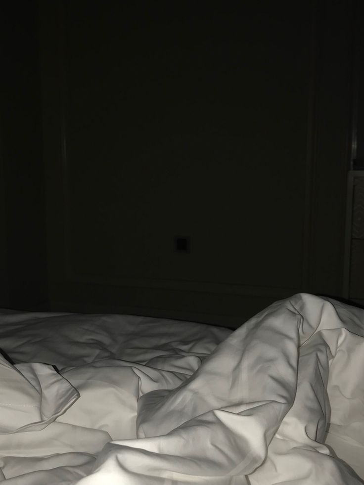 an unmade bed with white sheets in a dark room