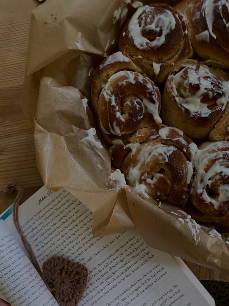 cinnamon buns with icing in a basket next to an open book