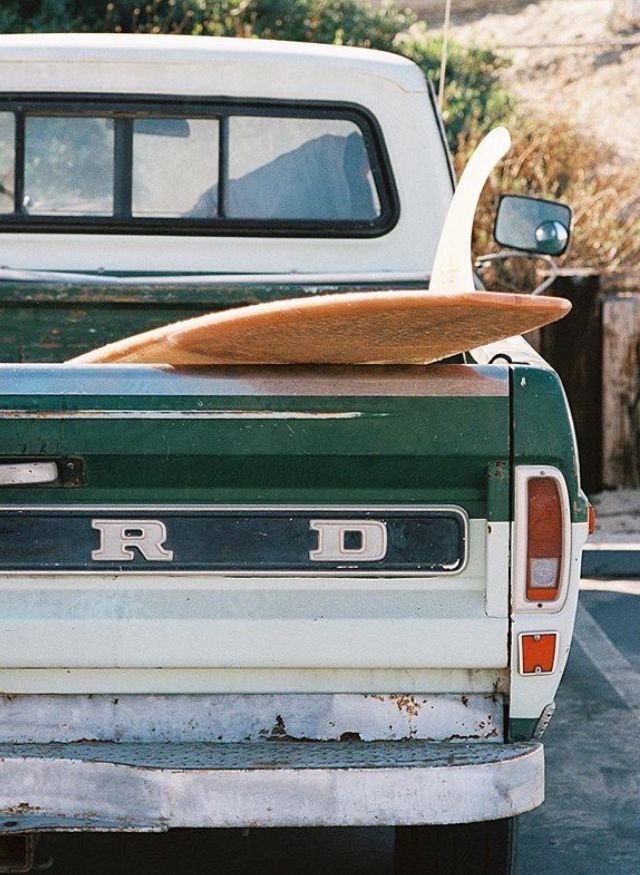 an old truck with a surfboard on the back of it's flat bed