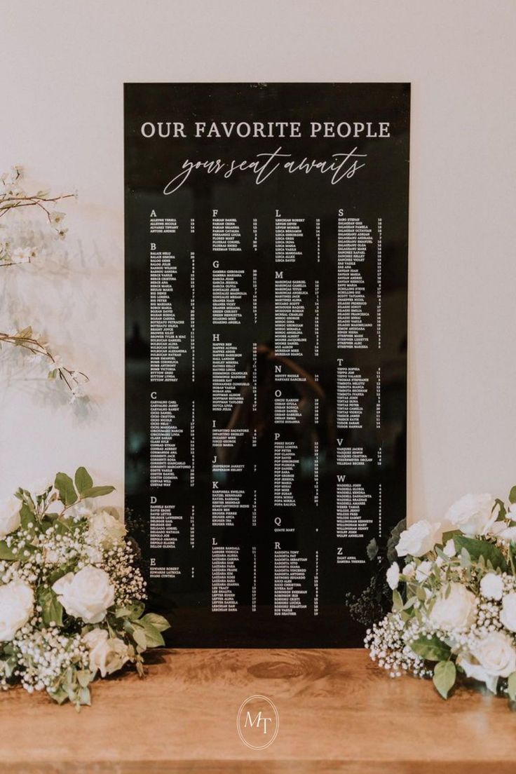 wedding seating chart with white flowers and greenery on the table next to each other