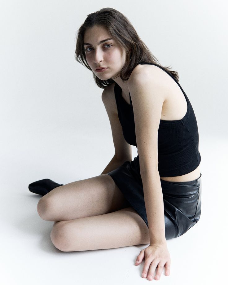 a young woman sitting on the floor wearing black clothes and posing with her legs crossed