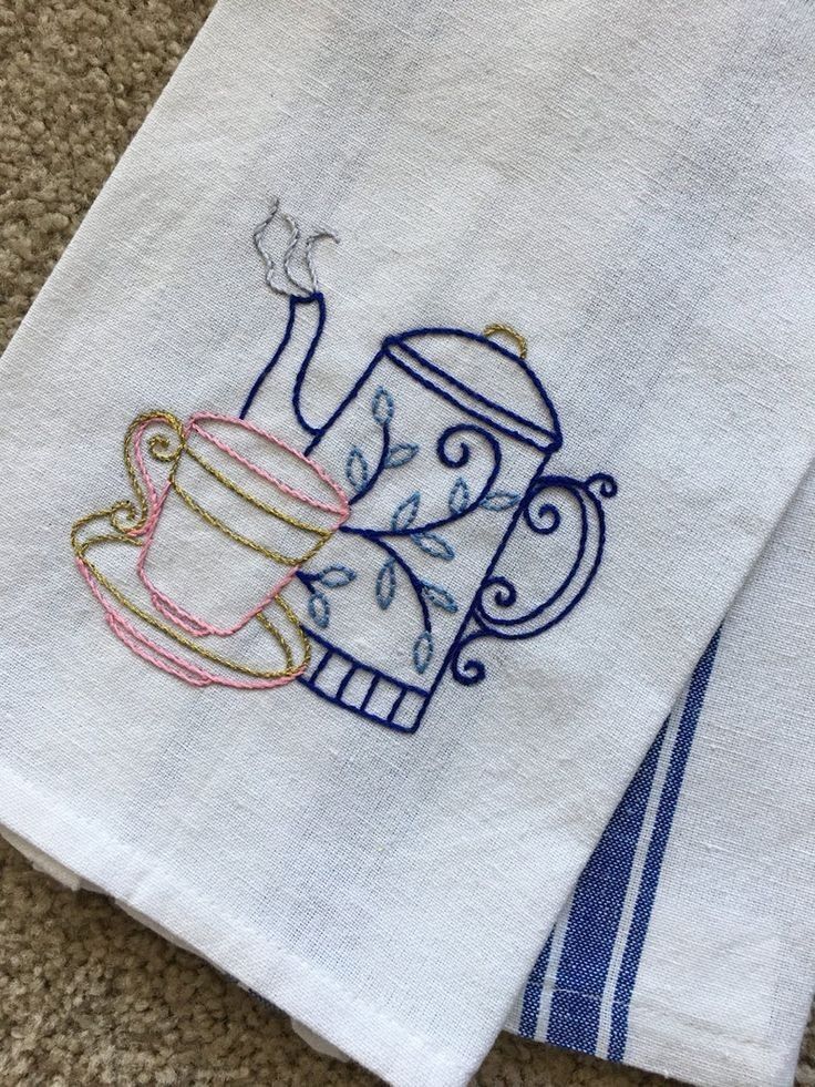 two towels with embroidered tea cups on them sitting on the floor next to each other