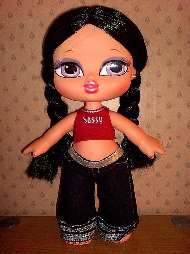 an image of a doll with big eyes and black hair standing on a wooden table