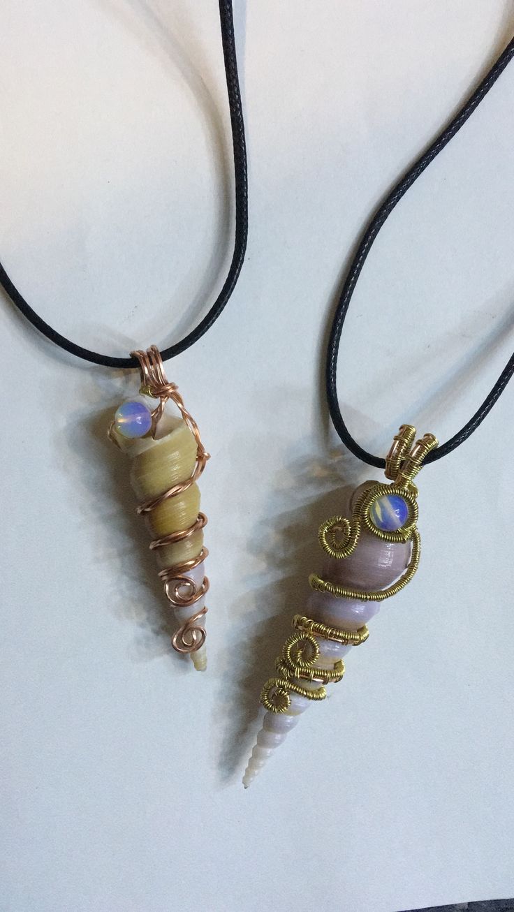 two necklaces that are sitting on a white surface together, one has a glass bead and the other has a wire wrapped around it