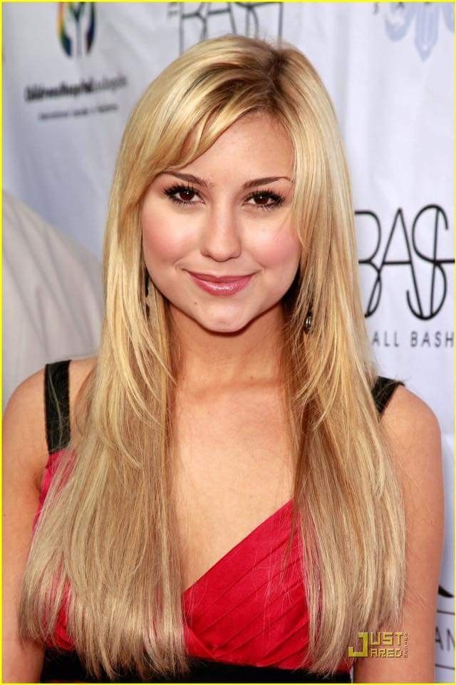 a woman with long blonde hair and bangs smiling at the camera, wearing a red dress