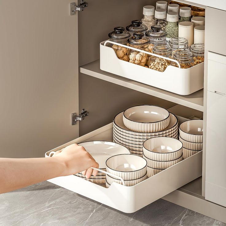 a person is reaching for dishes in a drawer on the side of a kitchen counter