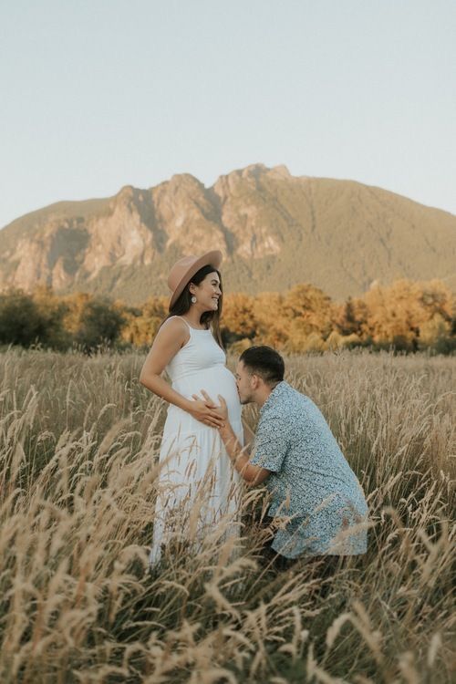 a man kneeling down next to a pregnant woman in a field with mountains in the background