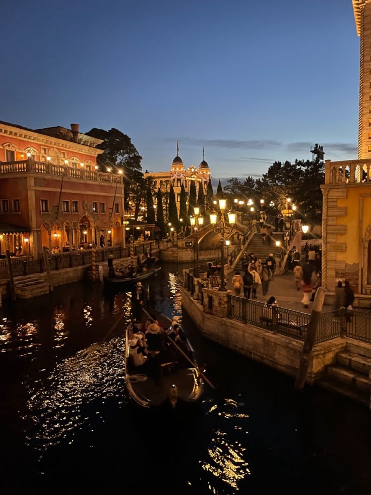 a boat floating down a river next to a tall building at night with lots of lights on