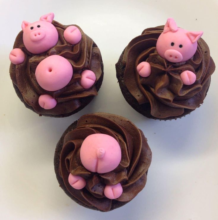 three cupcakes with pigs in the middle on top of each other and chocolate frosting