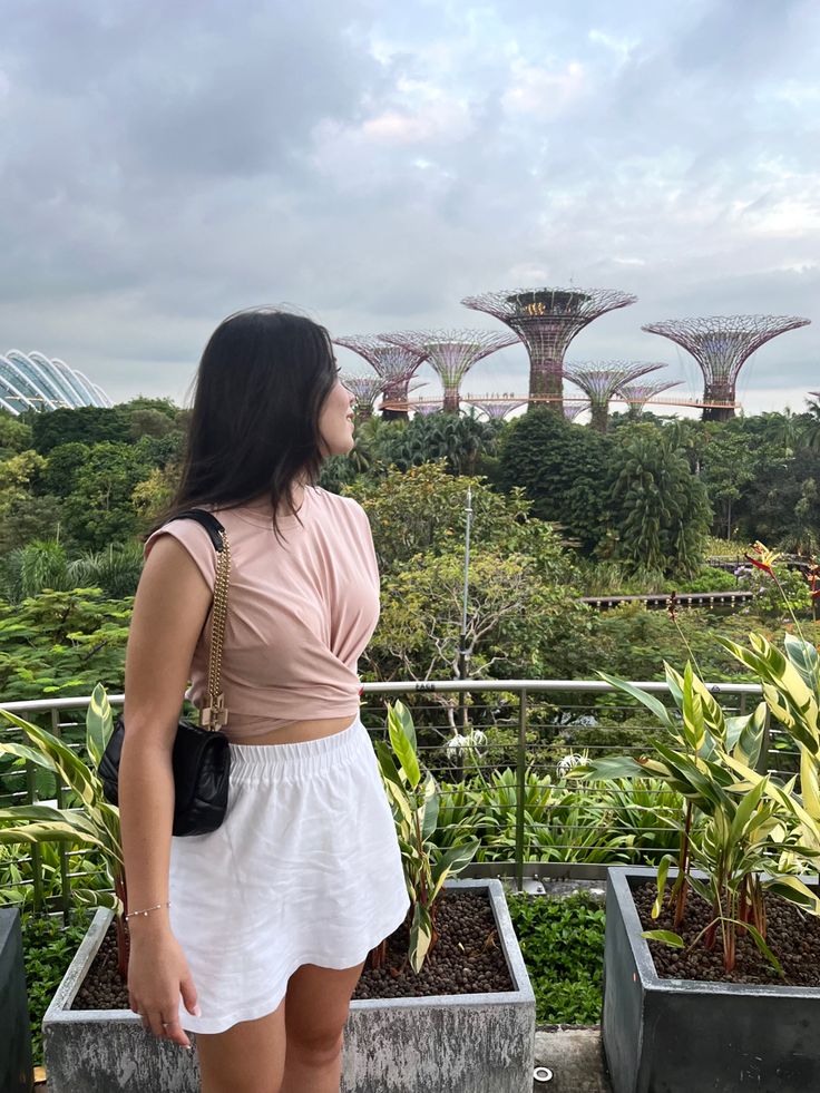 a woman is standing in front of some plants and looking out at the gardens by the bay