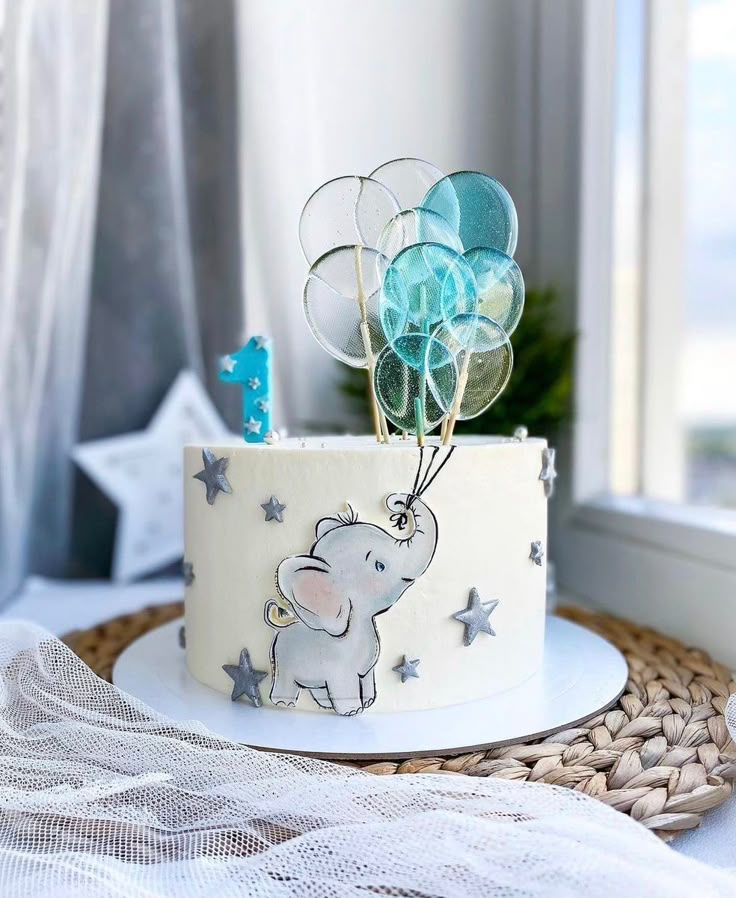 a white cake decorated with an elephant and balloons