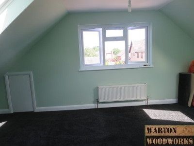 an empty room with black carpet and a window on the far wall, next to a radiator