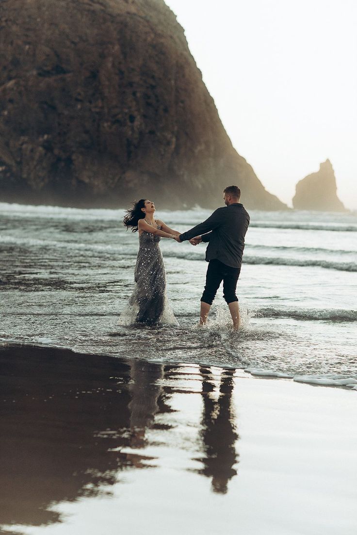 a man and woman are holding hands in the water at the beach near some cliffs