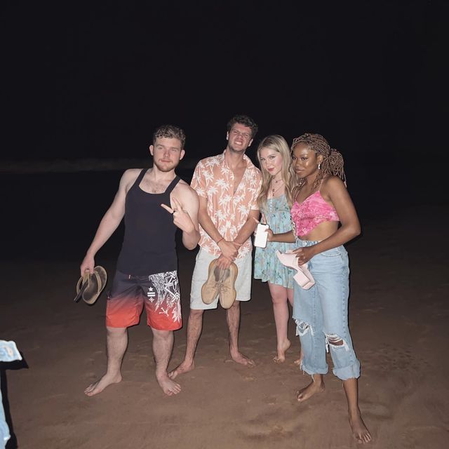 four people standing on the beach at night with one holding a frisbee in his hand