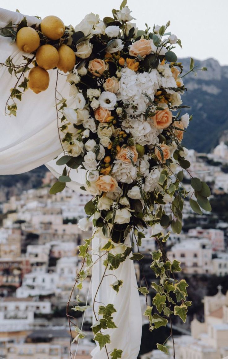 an orange and white floral arrangement on the top of a wedding arch in front of a cityscape