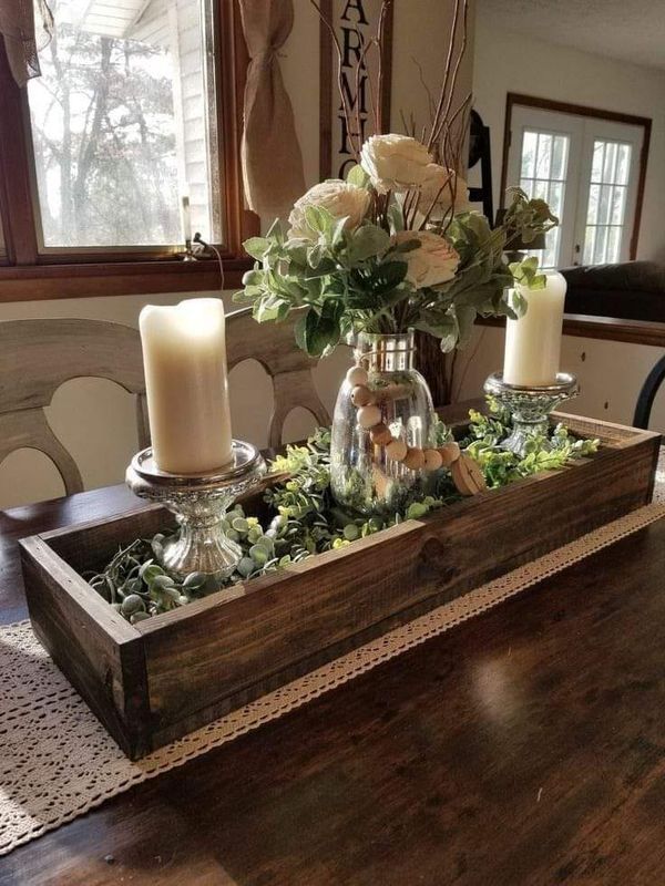 a wooden tray with candles and flowers in it on a dining room table next to a window