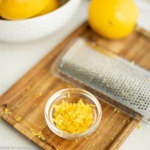 a wooden cutting board topped with lemons next to a bowl of grated cheese