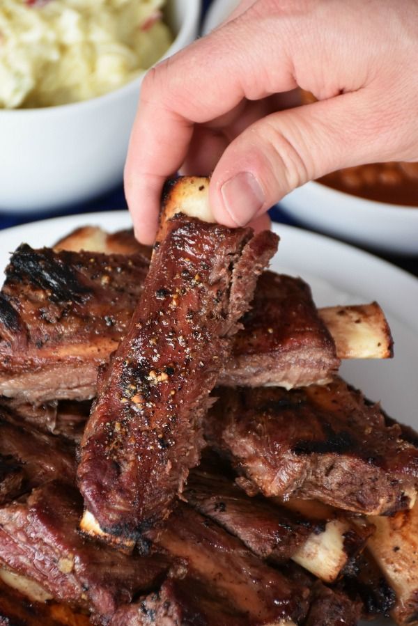 a person is picking up some meat from a plate with other foods in the background