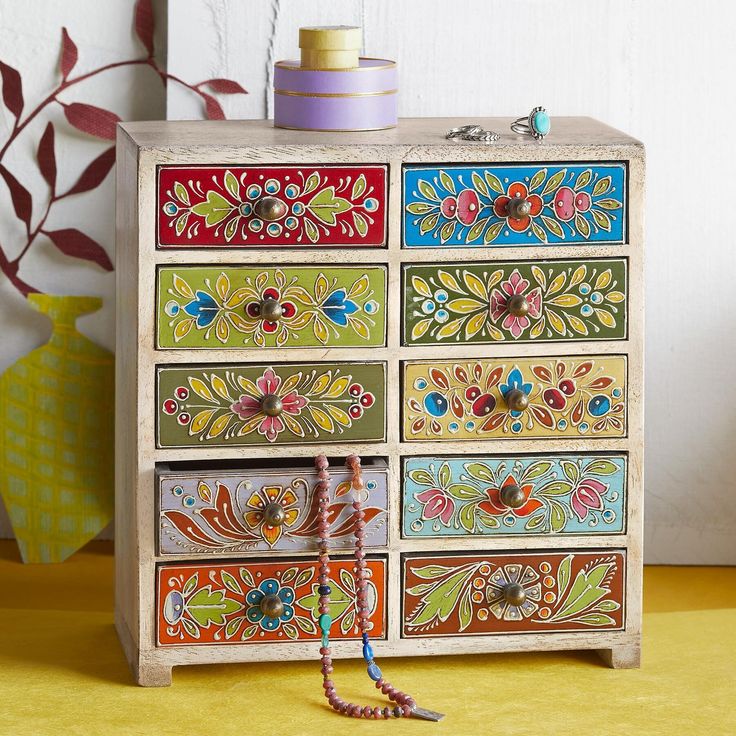 a multicolored dresser with many drawers and beads on the bottom drawer, next to a potted plant