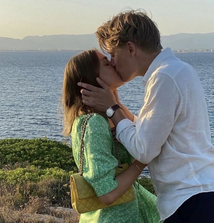 a man and woman kissing in front of the ocean