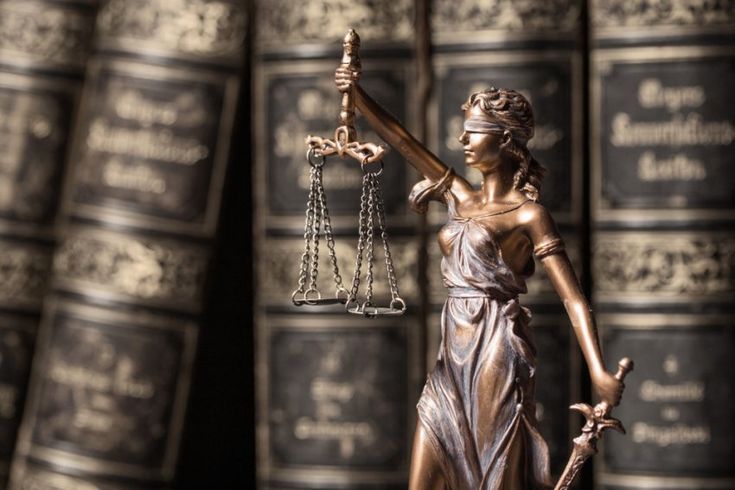 a statue of lady justice holding the scales of justice in front of some law books