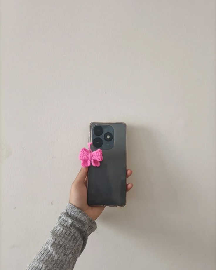 a person holding up a cell phone with a pink bow on it's back