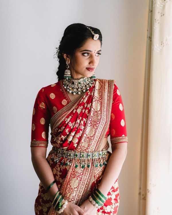 a woman in a red and gold bridal outfit standing next to a window with her hands on her hips