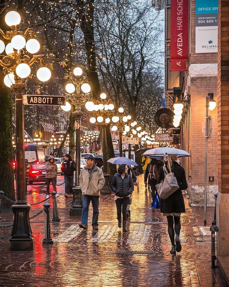 people walking down the street with umbrellas on a rainy day at night in an urban area