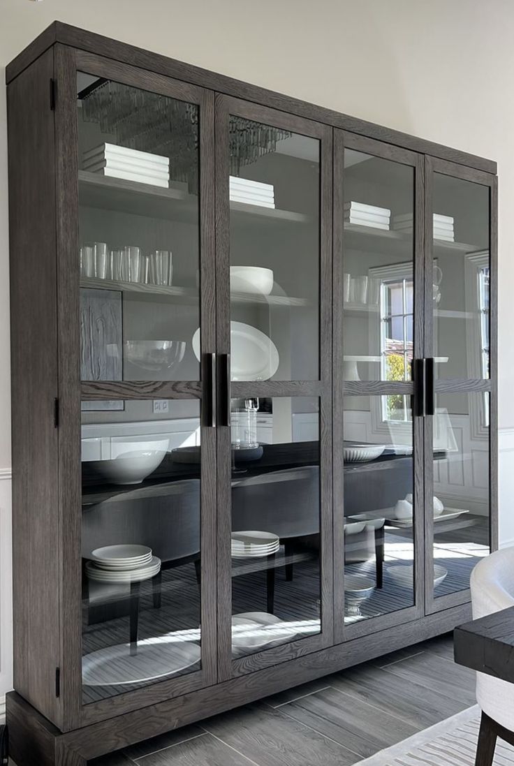 a dining room table and chairs in front of a glass cabinet with plates on it