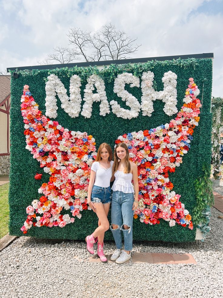 two girls standing in front of a flower wall with the word wash written on it