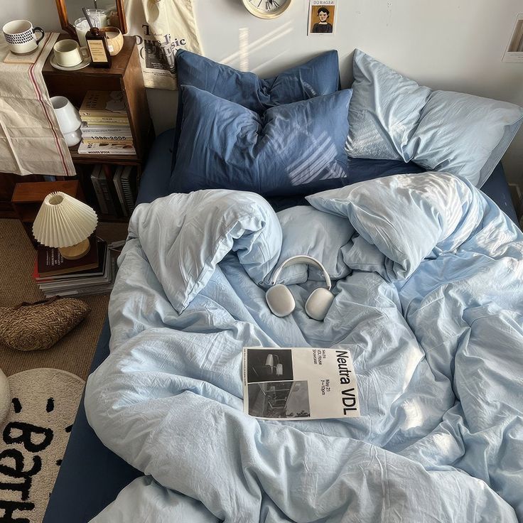 an unmade bed with blue sheets and headphones on it, in a bedroom