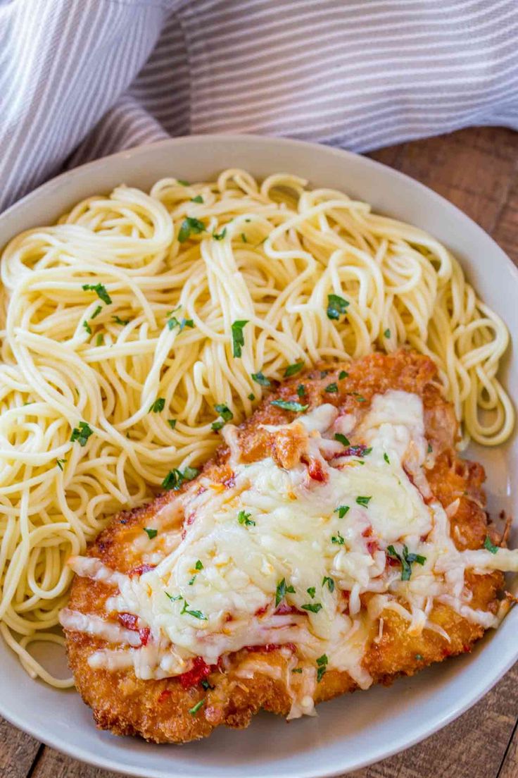 chicken parmesan with pasta in a white bowl on a wooden table next to a fork