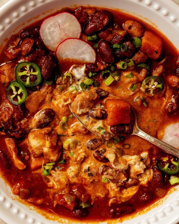 a white bowl filled with meat and vegetables next to a spoon on top of a table