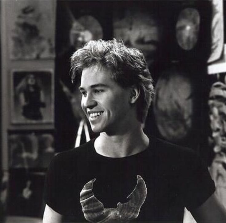 black and white photo of young man smiling in room with art work on the wall