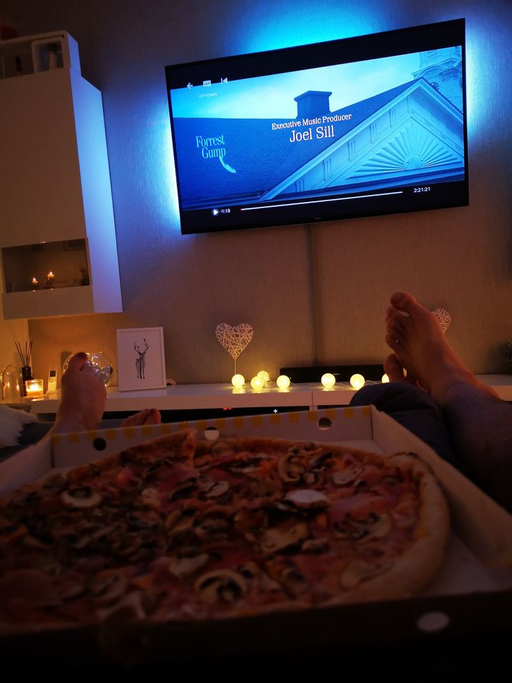 a person is sitting in front of a television with their feet up on a pizza