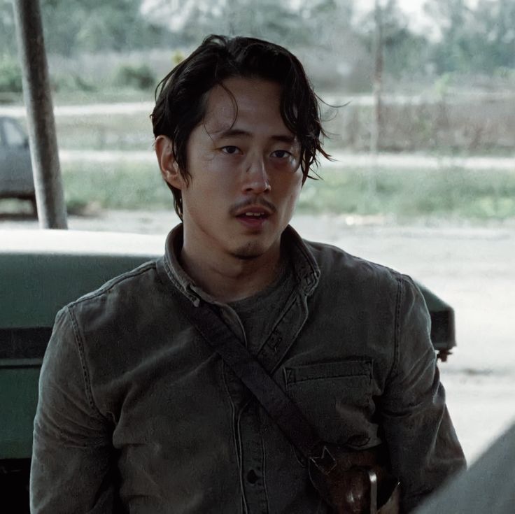 a young man standing in front of a green truck looking at the camera with an angry look on his face