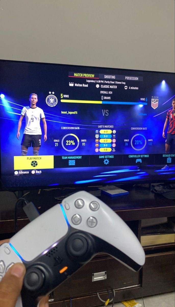 a person holding a video game controller in front of a flat screen tv with soccer on it