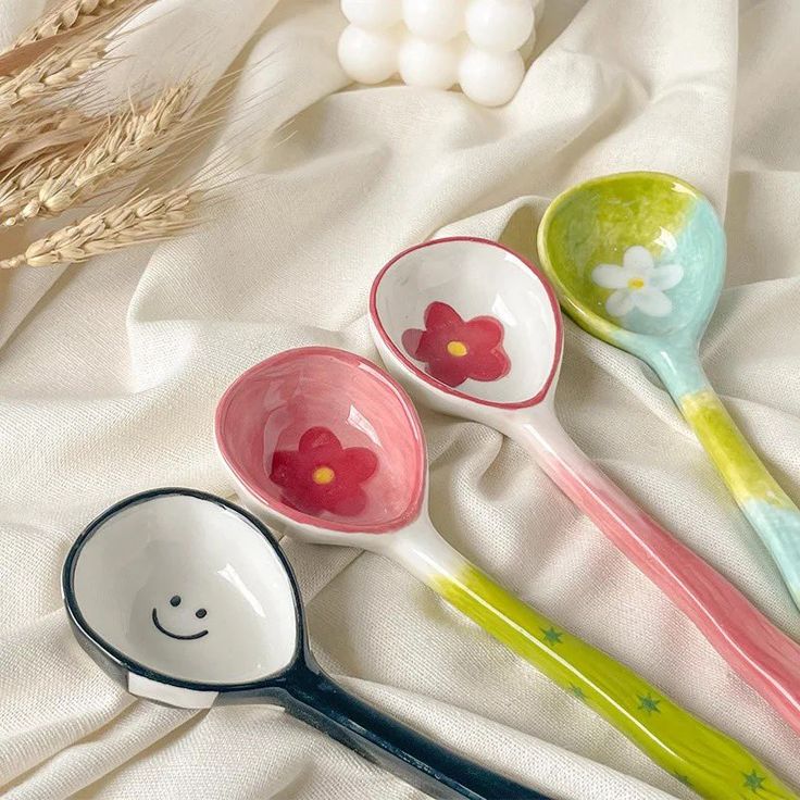 four spoons with flower designs on them sitting on a white cloth next to wheat stalks