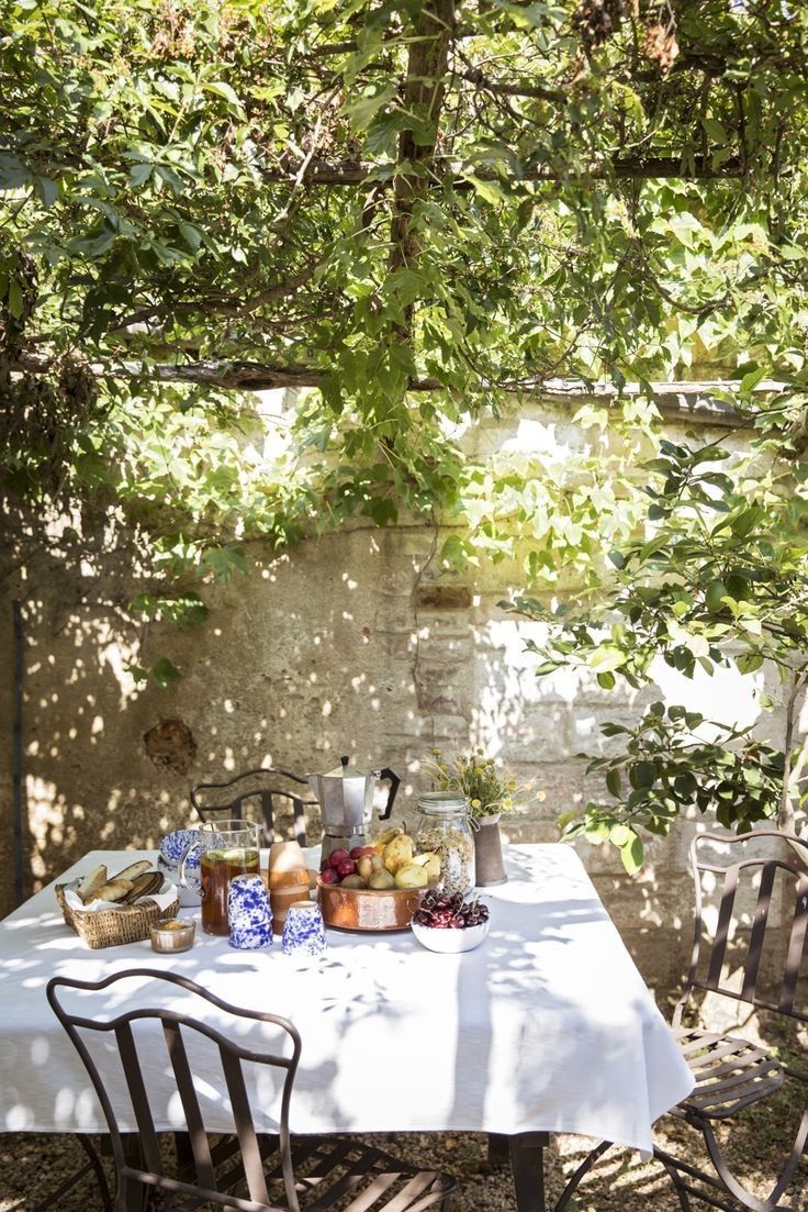 an outdoor table with food and drinks on it in the shade of a shady tree