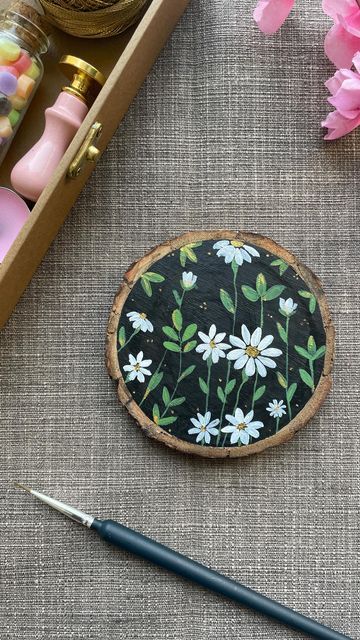 a wooden slice with daisies painted on it next to some crafting supplies and flowers