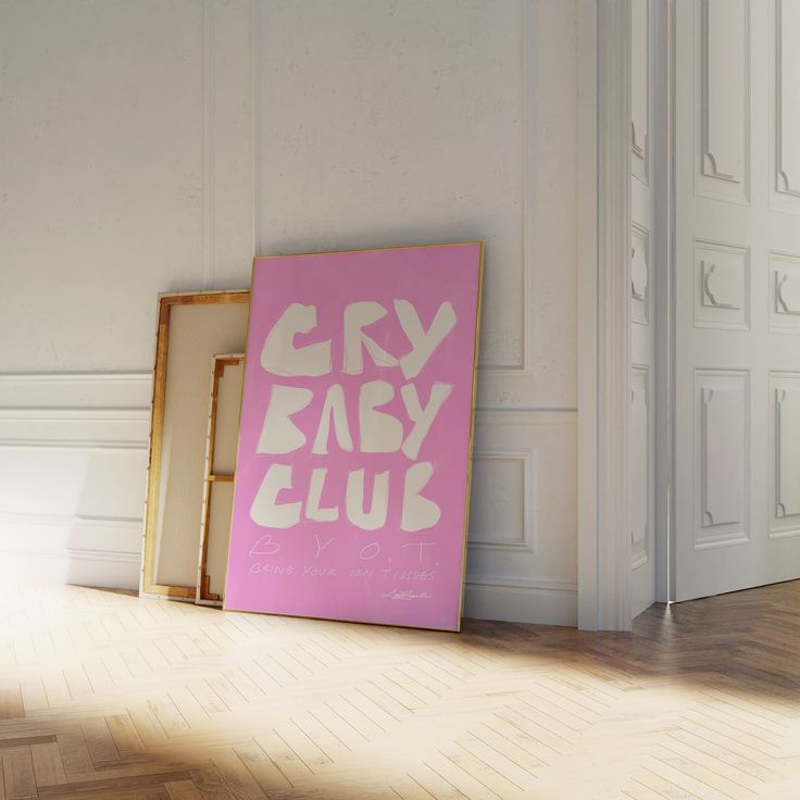 a pink sign sitting on top of a wooden floor next to a white wall and door