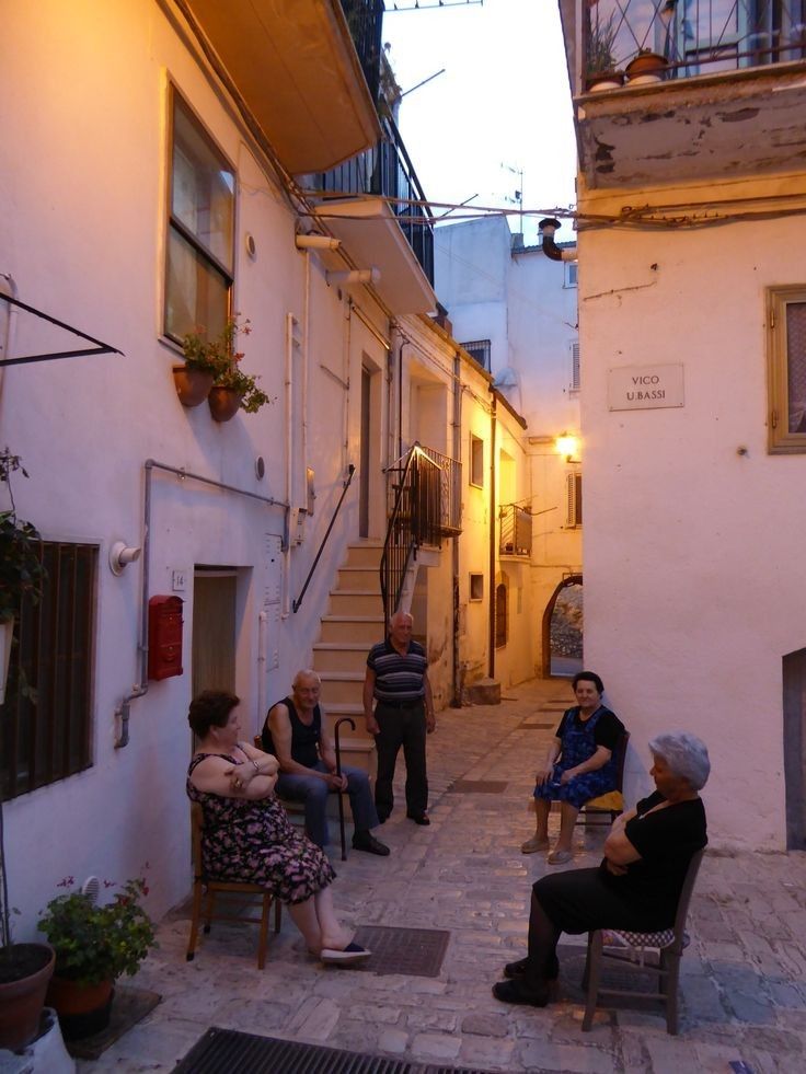 several people sitting on chairs in an alleyway at night, with one person walking up the stairs