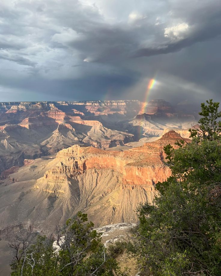 a rainbow shines in the sky over a canyon