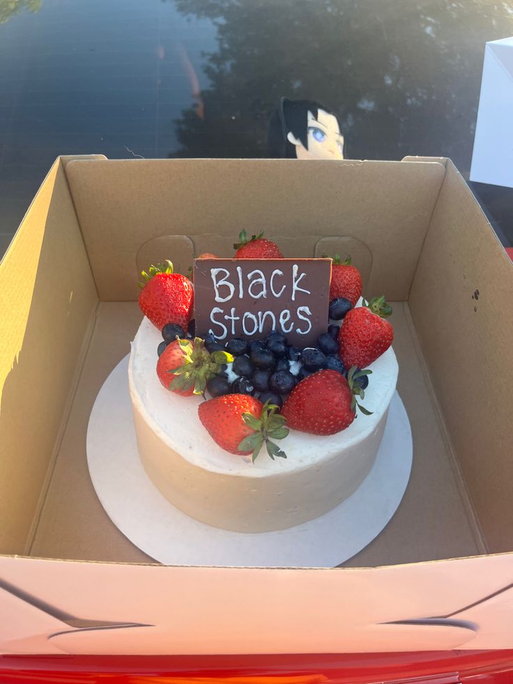 a white cake with strawberries and blueberries on top sits in a cardboard box