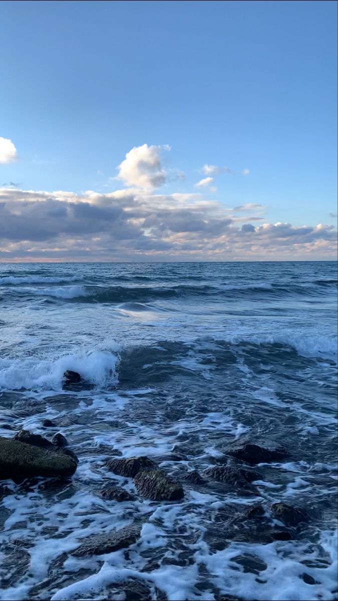 the ocean with waves crashing on rocks under a cloudy sky