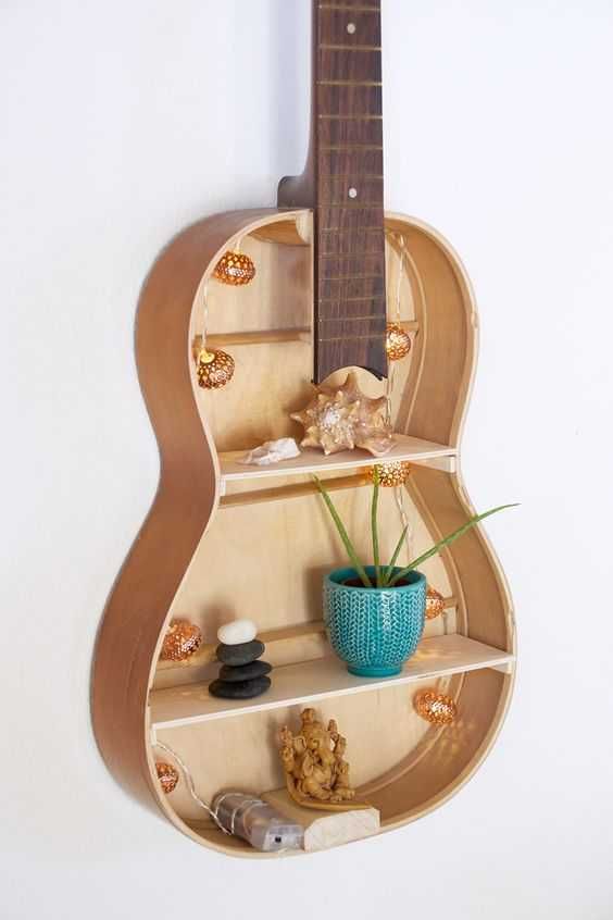 a guitar shaped shelf with flowers and rocks on it's sides, hanging from the wall