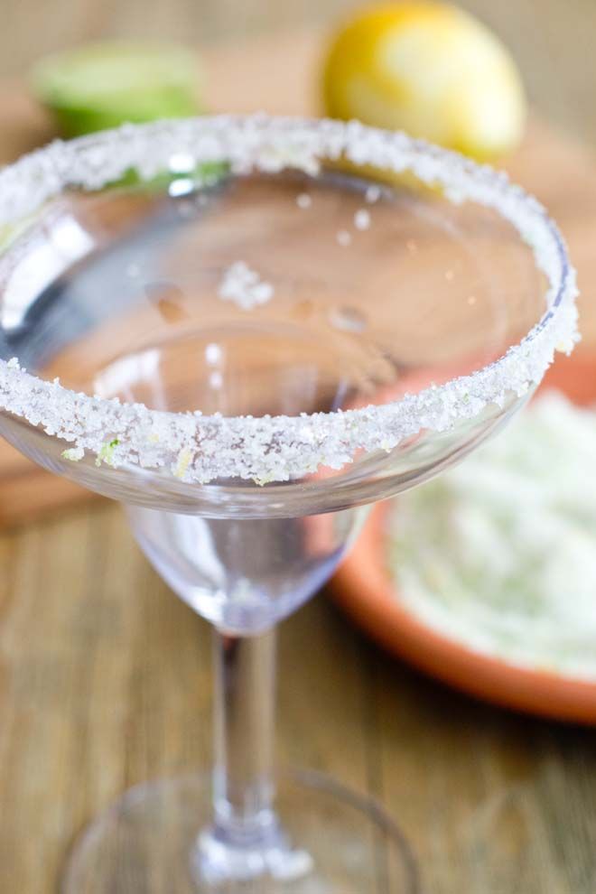 a close up of a margarita in a glass on a table with limes behind it