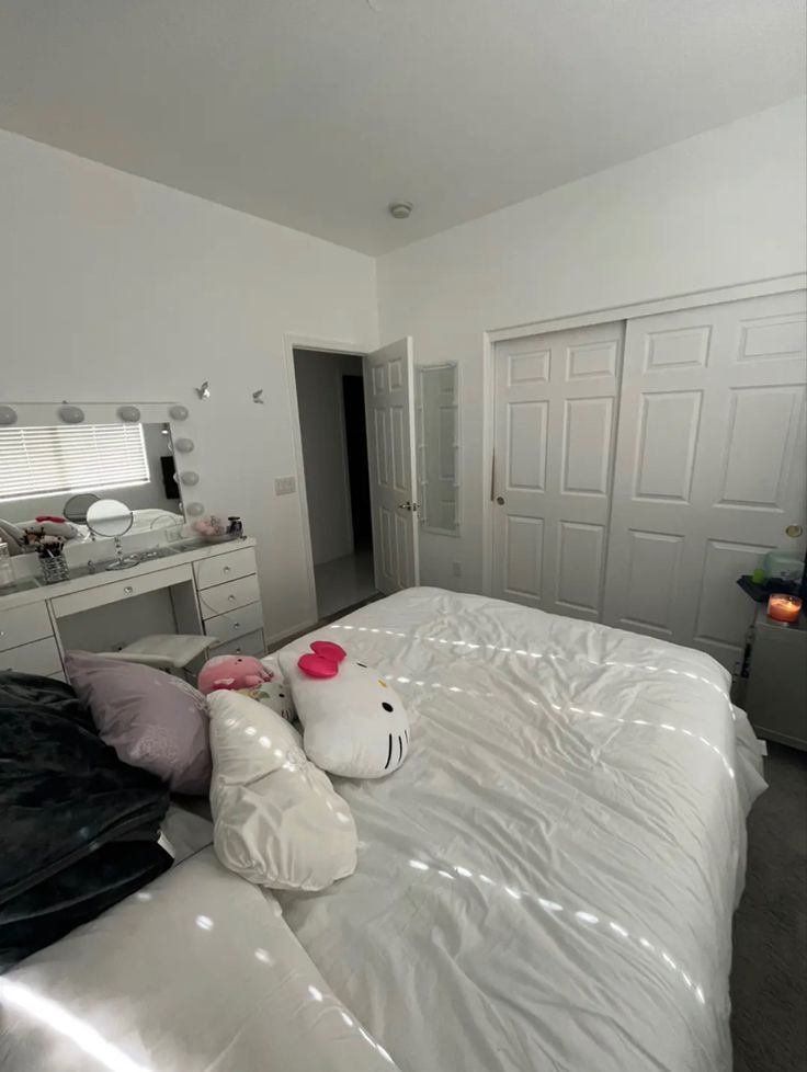 a white bed topped with lots of pillows next to a dresser and mirror in a bedroom